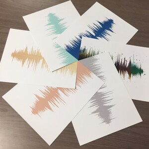 May include: Eight different sound wave prints in various colors, including blue, green, brown, gray, and peach. The prints are arranged in a circle on a wooden surface.