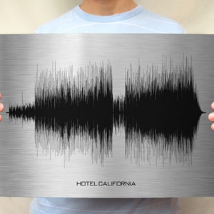 May include: A person holding a metal print with a black and white sound wave graphic and the text "HOTEL CALIFORNIA" printed below the graphic.