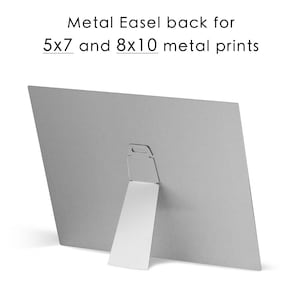 May include: Back of a metal print with a built-in easel stand. The stand is made of white metal and folds out to prop the print up. The print is designed to fit 5x7 and 8x10 metal prints.