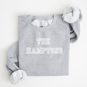 May include: Gray sweatshirt with white text that reads "THE HAMPTONS" in a collegiate font.