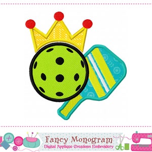 Puede incluir: Una bola de pickleball verde y negra con una pala amarilla y azul y una corona amarilla con detalles rojos. La imagen es para un diseño de bordado digital.