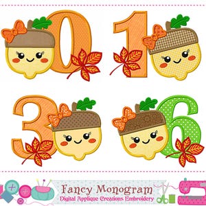 May include: Embroidered applique designs showing the numbers 0, 1, 3, and 6, each with a smiling cartoon acorn wearing a bow. The numbers are in orange and green, with autumn leaf accents. The design is labelled "Fancy Monogram".