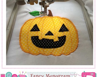 May include: A yellow pumpkin applique with white polka dots, featuring black fabric eyes, a nose, and a mouth with white polka dots. The pumpkin has a brown stem and a green leaf, all embroidered onto white fabric within an embroidery hoop.