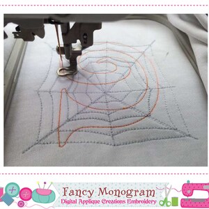 K&ouml;nnte beinhalten: Nahaufnahme einer Stickmaschine, die ein Spinnennetz-Design in orangefarbenem und grauem Garn auf wei&szlig;em Stoff stickt. Das Design ist ein stilisierter Buchstabe "P" mit einem Spinnennetz-Muster.