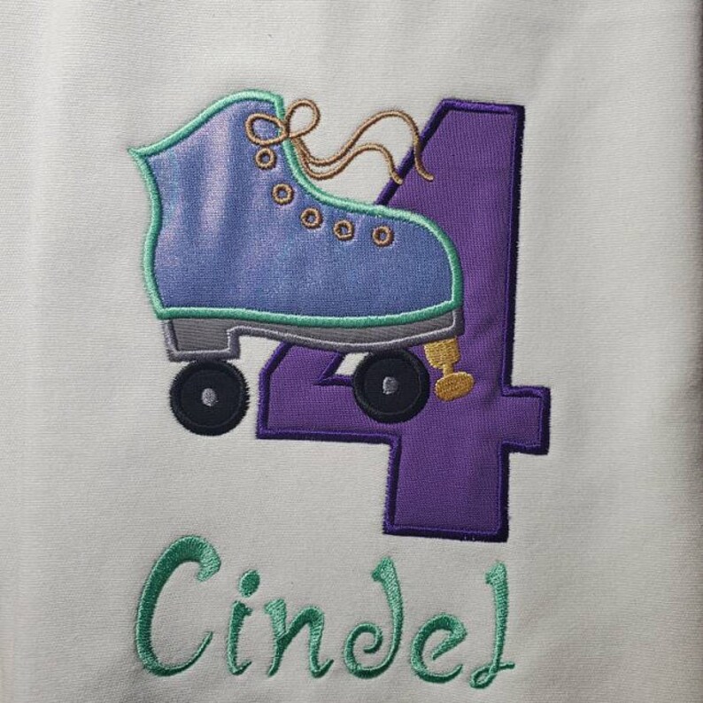 May include: Purple number four with a green and blue roller skate design. The name Cindel is embroidered in green below the number.
