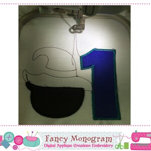 Puede incluir: Una m&aacute;quina de bordar bordando un dise&ntilde;o con el n&uacute;mero "1" en azul con contorno turquesa, y una forma negra sobre tela blanca. El texto "Fancy Monogram" es visible en la parte inferior.