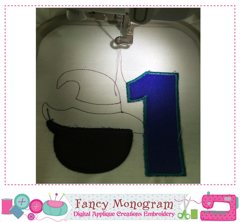 Puede incluir: Una m&aacute;quina de bordar bordando un dise&ntilde;o con el n&uacute;mero "1" en azul con contorno turquesa, y una forma negra sobre tela blanca. El texto "Fancy Monogram" es visible en la parte inferior.