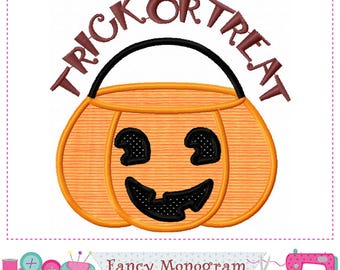 May include: An orange pumpkin-shaped candy bucket with a black handle and a black jack-o'-lantern face featuring two eyes and a wide, jagged smile. The text TRICK OR TREAT is embroidered in dark brown letters in an arc above the bucket.