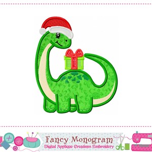 May include: A green dinosaur wearing a red Santa hat and carrying a green gift box with a red bow. The dinosaur has a friendly expression and is outlined in white. The image is a digital applique design.