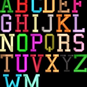 May include: A collection of twenty-eight embroidered letters of the alphabet, including duplicates, arranged in rows against a black background. Each letter features a distinct solid color, including green, red, blue, orange, brown, pink, purple, yellow, grey, and black, with a textured stitch pattern.
