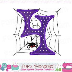 K&ouml;nnte beinhalten: Lilafarbener Buchstabe "L" mit wei&szlig;en Punkten, schwarz umrandet, der an einem schwarzen Spinnennetz mit einer schwarzen Spinne mit roten Augen h&auml;ngt. Der Text "Fancy Monogram" befindet sich unter dem Bild.