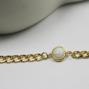 May include: A gold chain bracelet with a white opal gemstone in the center.
