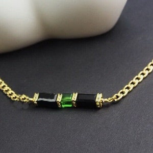 May include: A gold chain necklace with a black and green stone pendant.