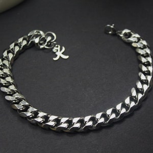 May include: A silver curb chain bracelet with a small silver charm that has the letter 'X' on it.