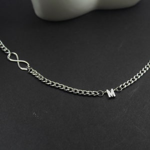 May include: A silver chain necklace with an infinity symbol charm and a letter 'M' charm.