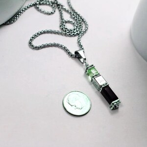 May include: A silver chain necklace with a pendant made of three stacked rectangular stones. The top two stones are green and the bottom stone is black.