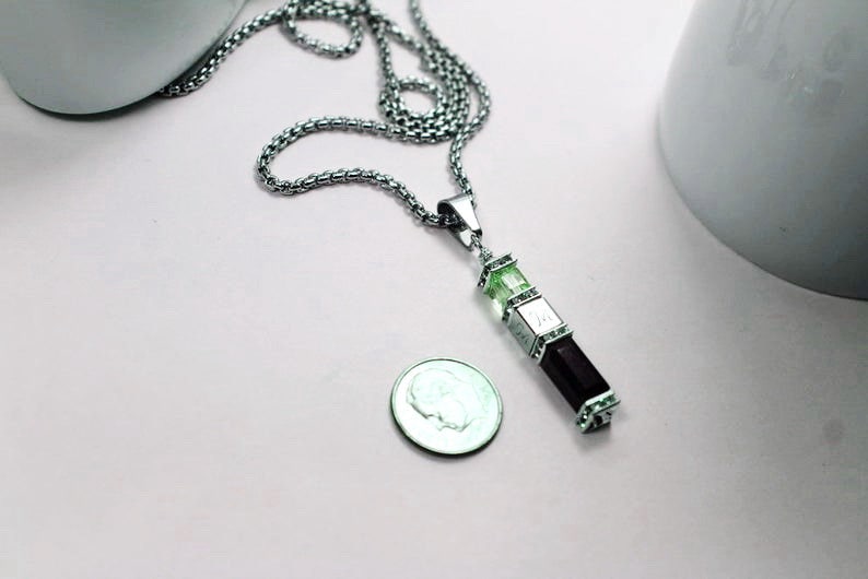 May include: A silver chain necklace with a pendant made of three stacked rectangular stones. The top two stones are green and the bottom stone is black.