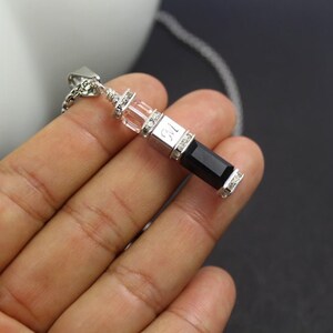 May include: A silver pendant necklace with a black rectangular stone and clear crystal accents. The pendant has the number "12" engraved on it.