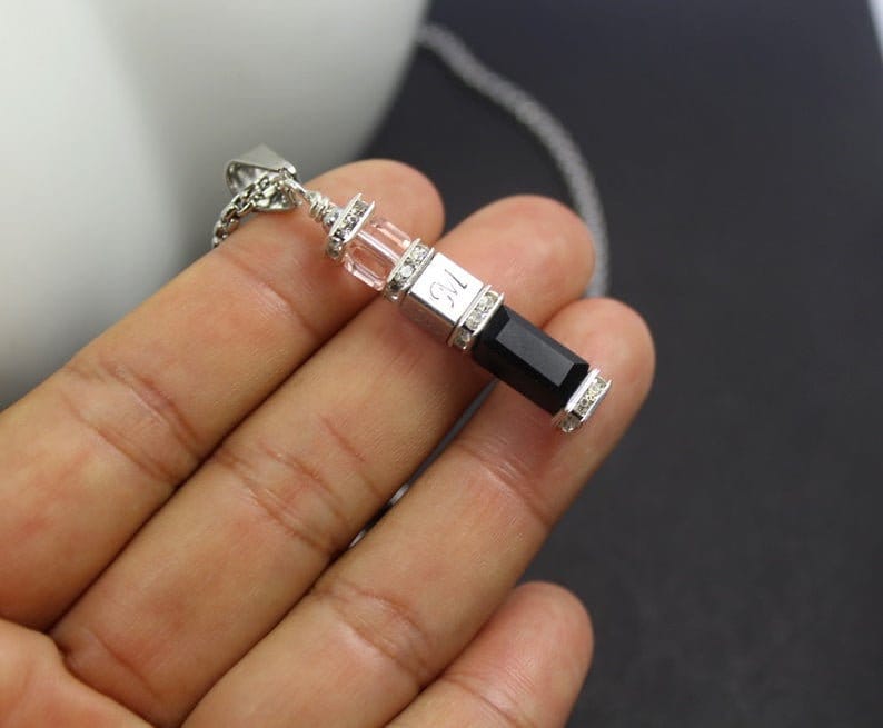 May include: A silver pendant necklace with a black rectangular stone and clear crystal accents. The pendant has the number "12" engraved on it.