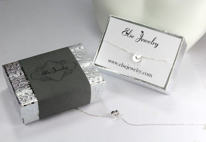 May include: A silver necklace with a small circle pendant, packaged in a gray box with the text "Else Jewelry" and a white box with the text "Else Jewelry" and the website address "www.elsejewelry.com".