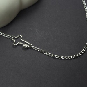 May include: A silver chain necklace with a cross-shaped clasp. The chain is a curb style and the clasp is a simple design.