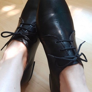 May include: A pair of black leather lace-up shoes with a rounded toe. The shoes are worn and the laces are tied.