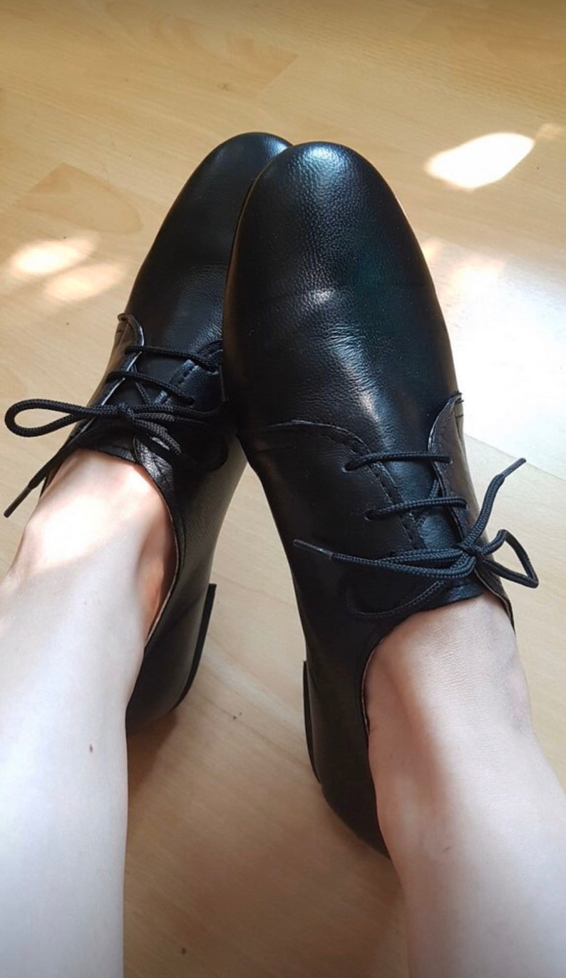 May include: A pair of black leather lace-up shoes with a rounded toe. The shoes are worn and the laces are tied.