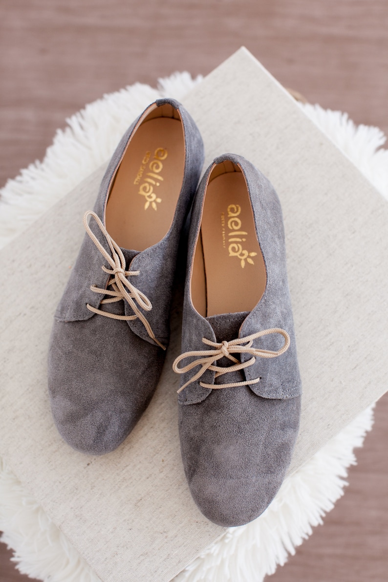 May include: A pair of gray suede lace-up shoes with tan laces. The shoes have the brand name "aellia" printed on the inside of each shoe.
