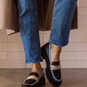 May include: Black leather loafers with a white and light blue trim. The loafers have a chunky platform sole.