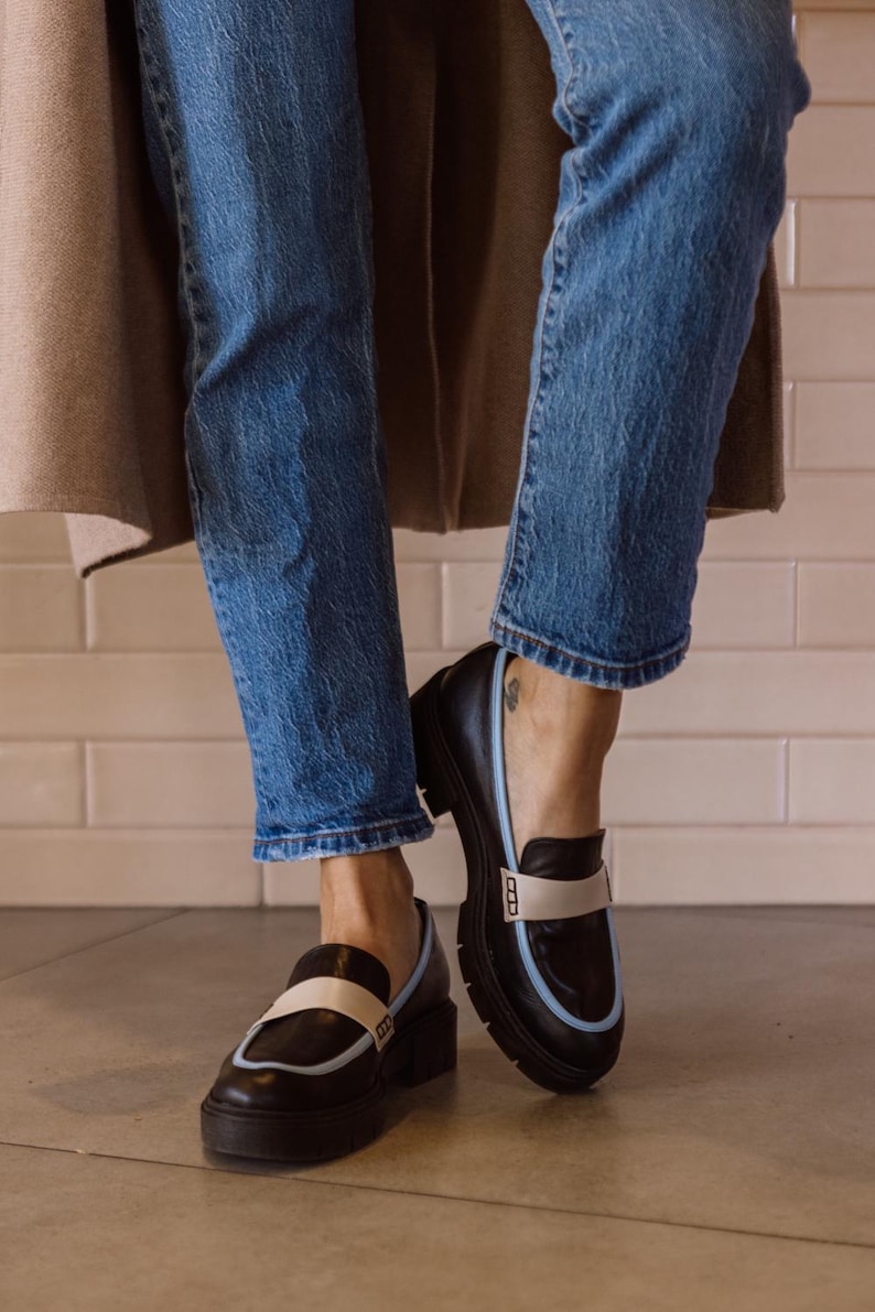 May include: Black leather loafers with a white and light blue trim. The loafers have a chunky platform sole.