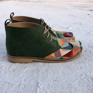 May include: Green suede ankle boots with a colourful geometric pattern on the toe and heel. The boots have a lace-up closure and a brown sole.
