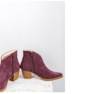 Pu&ograve; includere: Un paio di stivaletti in suede bordeaux con punta a punta e tacco basso a blocco. Gli stivaletti hanno una cerniera all'interno di ogni stivaletto.