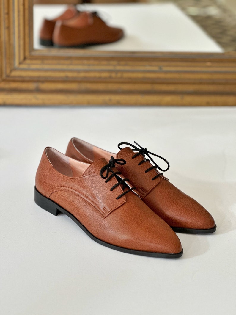 May include: A pair of brown leather lace-up shoes with a pointed toe. The shoes have a black lace and a black sole.