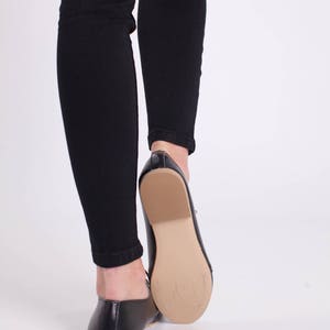 May include: A pair of black leather flats with a pointed toe and a low heel. The shoes are worn by a person wearing black jeans.