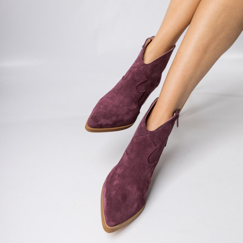 Pu&ograve; includere: Un paio di stivaletti in suede bordeaux con punta a punta e design in stile cowboy.