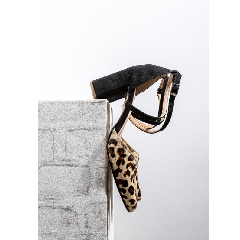 May include: Black heeled sandals with a leopard print design. The sandals have a thick strap across the ankle and a buckle closure.