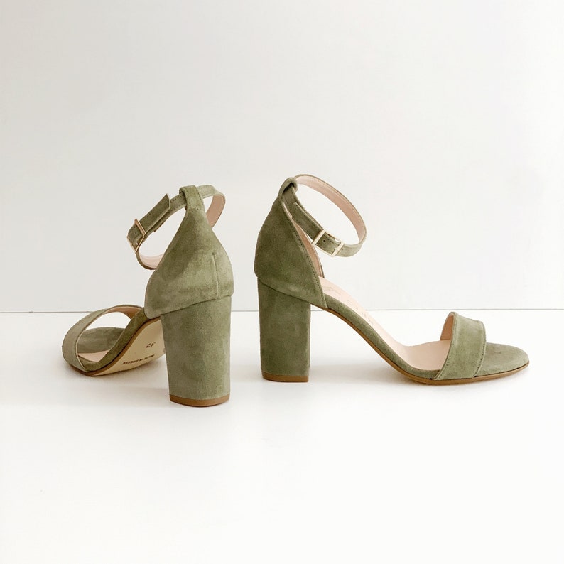 May include: A pair of green suede heeled sandals with ankle straps. The sandals have a block heel and an open toe.