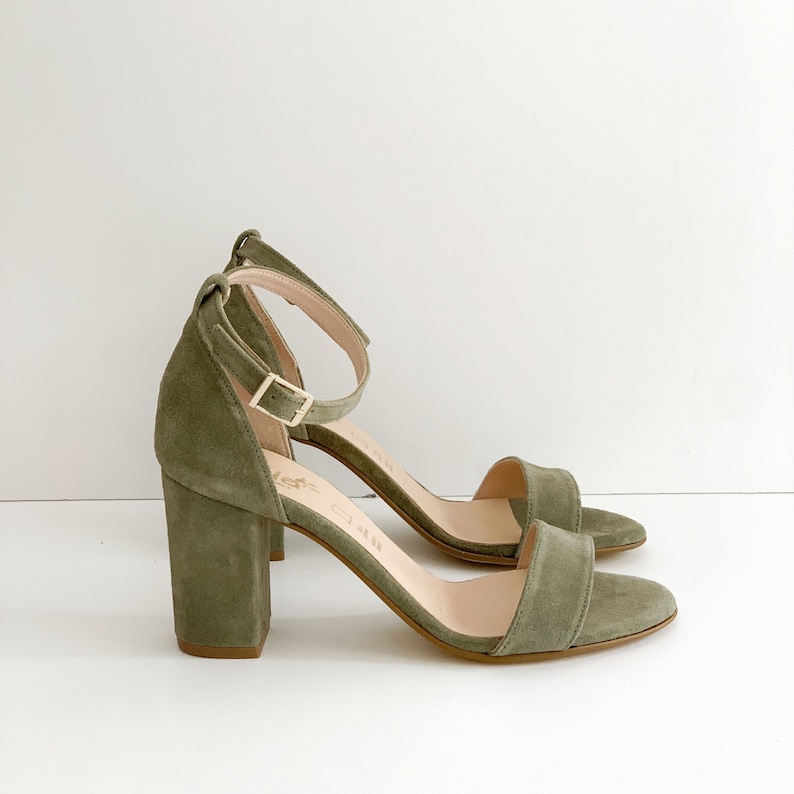 May include: A pair of olive green suede heeled sandals with an ankle strap and a block heel.