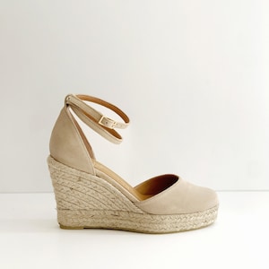 May include: Beige suede wedge sandals with an ankle strap and a rope platform sole.
