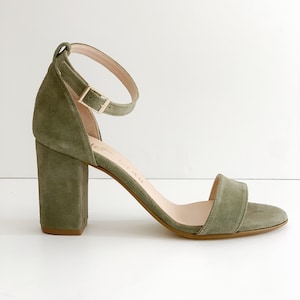 May include: Green suede heeled sandals with an ankle strap and a buckle closure. The heels are block shaped and about 3 inches tall.