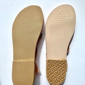 May include: Close-up of the soles of two sandals. The left sandal has a rubber sole with a textured pattern. The right sandal has a leather sole with a brick-like pattern.