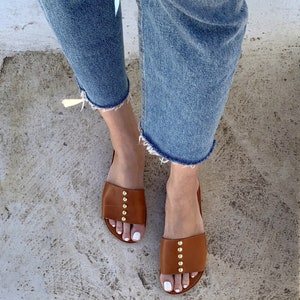 May include: A pair of brown leather sandals with gold studs. The sandals have a simple design and are perfect for summer.