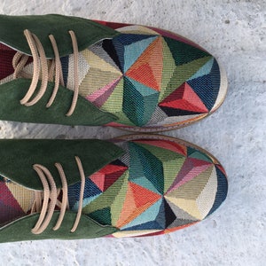 May include: A pair of green suede and fabric shoes with a geometric pattern in shades of red, blue, green, yellow, and orange.
