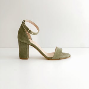 May include: Green suede heeled sandals with an ankle strap and a block heel.