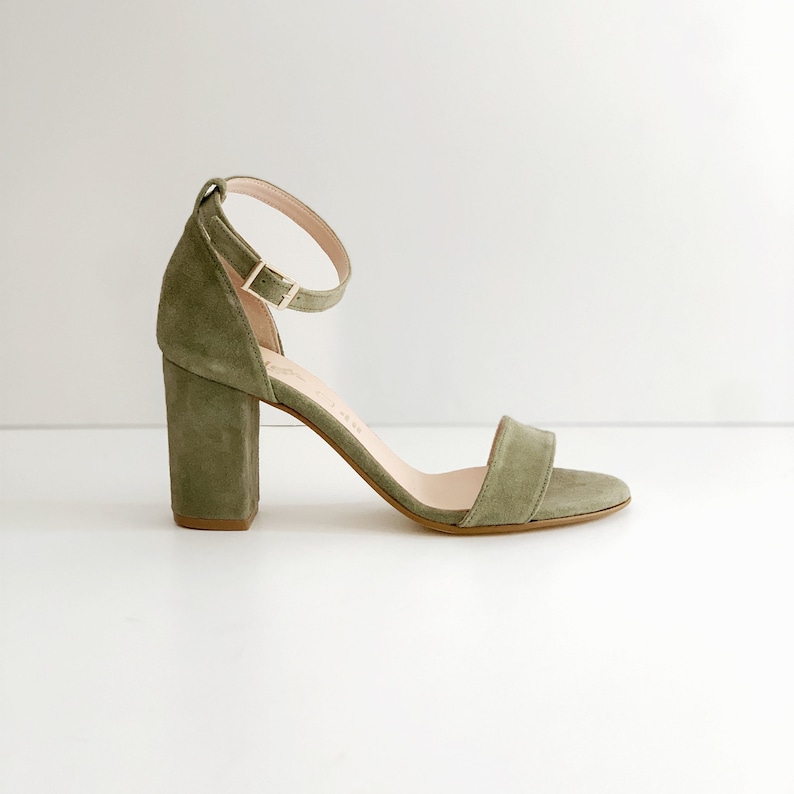 May include: Green suede heeled sandals with an ankle strap and a block heel.