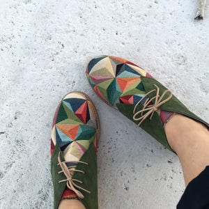 May include: A pair of green suede ankle boots with colourful geometric patterned fabric on the toe. The laces are a light brown colour.