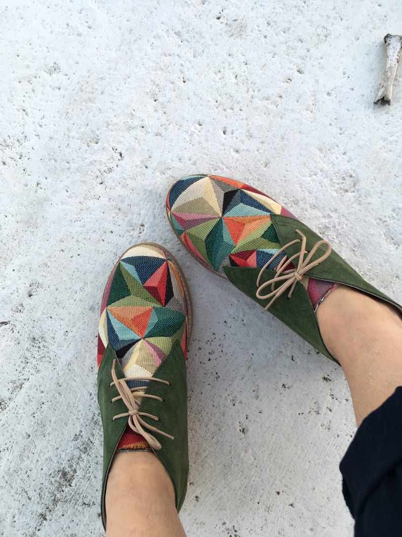May include: A pair of green suede ankle boots with colourful geometric patterned fabric on the toe. The laces are a light brown colour.
