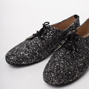 May include: A pair of black glitter lace-up shoes. The shoes have a pointed toe and a low heel.