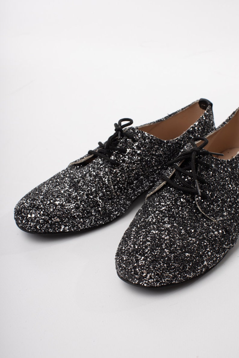 May include: A pair of black glitter lace-up shoes. The shoes have a pointed toe and a low heel.