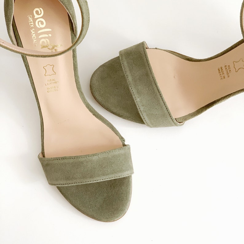 May include: A pair of green suede heeled sandals with ankle straps. The sandals have a simple design and are made of real leather. The label on the sandal reads "aellia" and "Green Sandal".